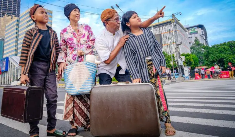 A family in traditional Javanese clothing crosses a street in Jakarta, suggesting a cultural journey.