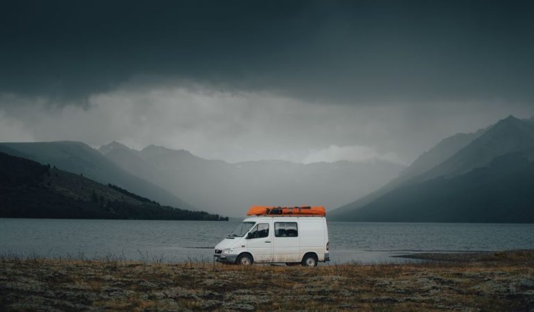 White campervan parked by a misty mountain lake under dramatic cloudy skies, perfect for travel adventures.
