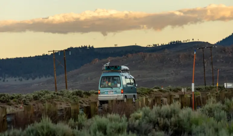 A camper van drives through a desert landscape at sunset